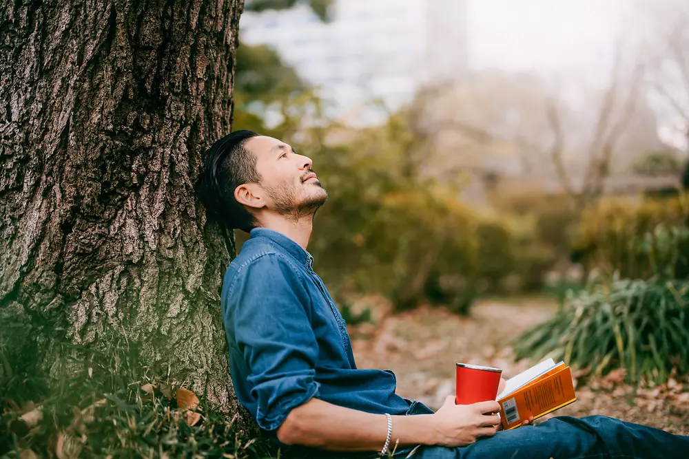 Чоловік із книжкою, який спирається на дерево